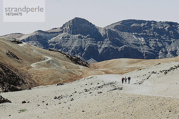 Drei Wanderer wandern auf einem Pfad in einer felsigen und vulkanischen Landschaft