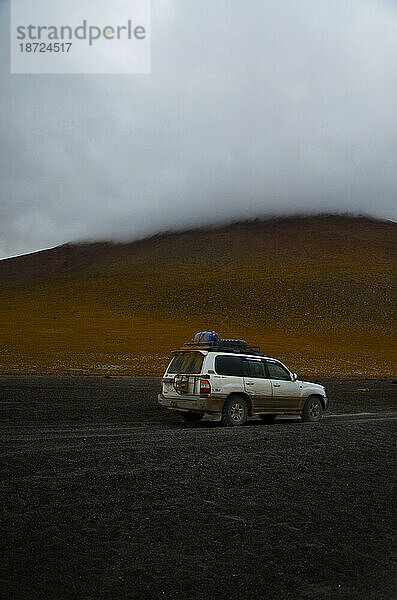Schlammiges Auto vor einem geheimnisvollen  wolkigen Berg in Bolivien