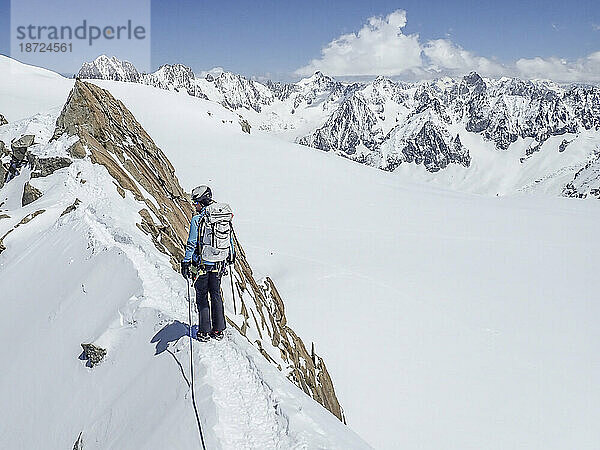 Eine Bergsteigerin blickt von einem exponierten Schneegrat in den Alpen zurück