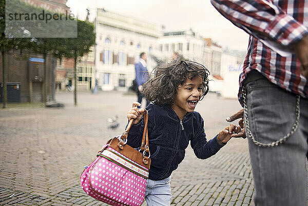 Süßes kleines schwarzes Mädchen rennt auf einem Platz in der Stadt um ihren Vater herum