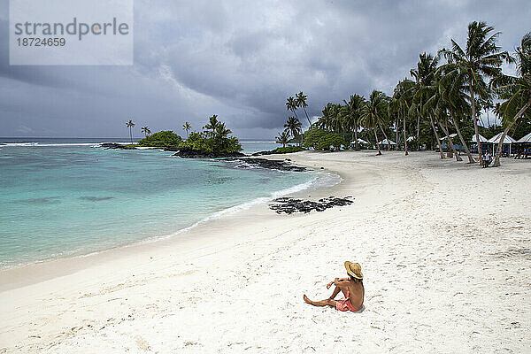 Ein Mann mit Hut und Badeanzug am Sandstrand von Samoa