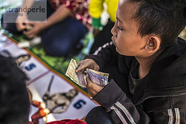 Es passiert während eines großen Dorffestes. Erwachsene und Kinder spielen mit dem Bargeldkurs. Dies trotz der Tatsache  dass Indonesien ein muslimisches Land ist und Glücksspiele verboten sind