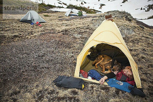 Ein junger Mann schläft in seinem Zelt und kuschelt mit seinem Hund im Camp am Parika Lake  Never Summer Wilderness  Colorado.