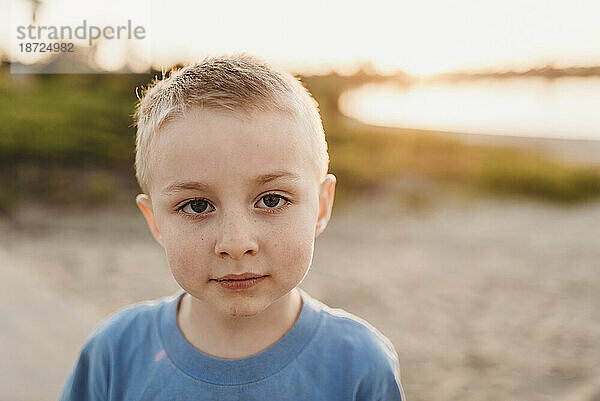 Porträt eines Jungen im schulpflichtigen Alter am Strand bei Sonnenuntergang im Gegenlicht