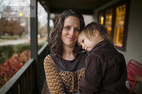Eine lächelnde Mutter steht draußen mit einem kleinen Kind im Arm