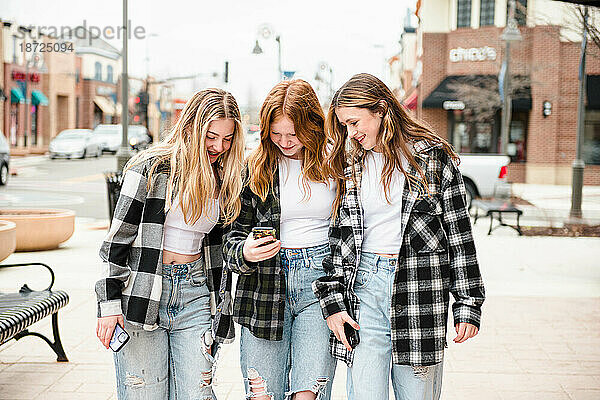 Drei schöne Teenager-Mädchen schauen auf ein Handy.