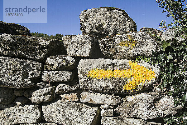 Ein gelber Pfeil auf einer alten Steinmauer weist Pilgern den Weg auf dem Jakobsweg in Galizien  Spanien.
