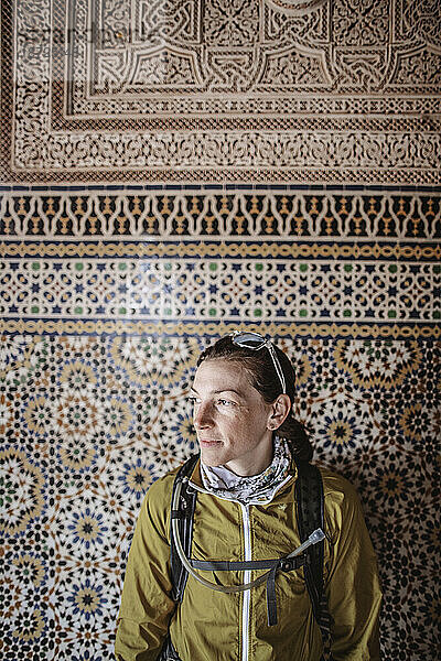 A caucasian woman stands in front of a mosaic in a casbah  Morocco