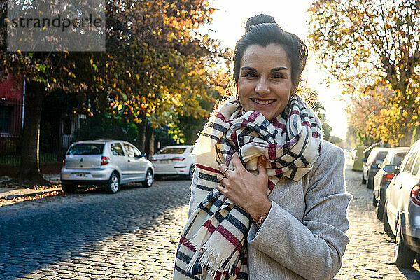 Porträt einer lächelnden jungen Frau mit Schal  die auf der Straße steht