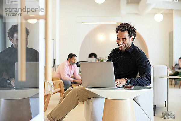 Lächelnder Geschäftsmann benutzt Laptop  während er auf dem Sofa im Café sitzt