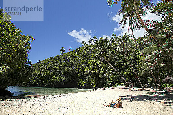 Ein Mann bräunt sich an einem sonnigen Tag am tropischen Strand unter Palmen
