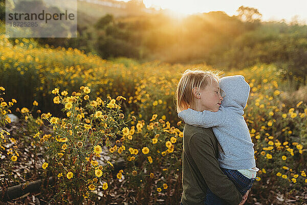 Kleiner Junge umarmt seine kleine Schwester bei Sonnenuntergang liebevoll