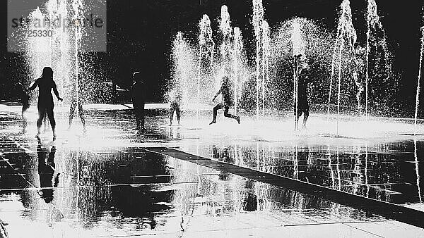 Kinder springen und genießen auf einem öffentlichen Platz mit Springbrunnen