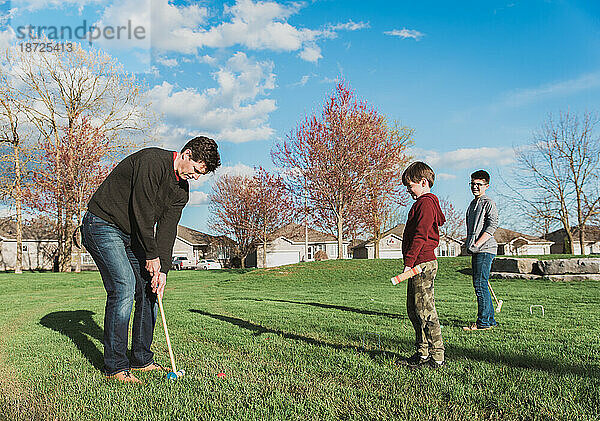Vater und seine beiden Jungen spielen gemeinsam Krocket in einem Park.
