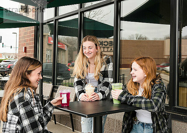 Drei glückliche Teenager-Mädchen trinken vor einem Café etwas.