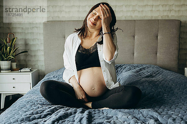 Schwangeres Mädchen sitzt mit geschlossenen Augen auf dem Bett