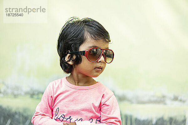 Nettes kleines Mädchen  das eine modische Sonnenbrille trägt und Spaß macht