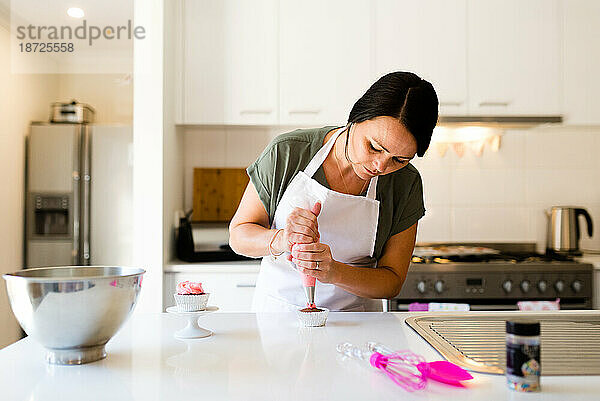 Eine Frau dekoriert in ihrer Küche einen Cupcake mit Zuckerguss