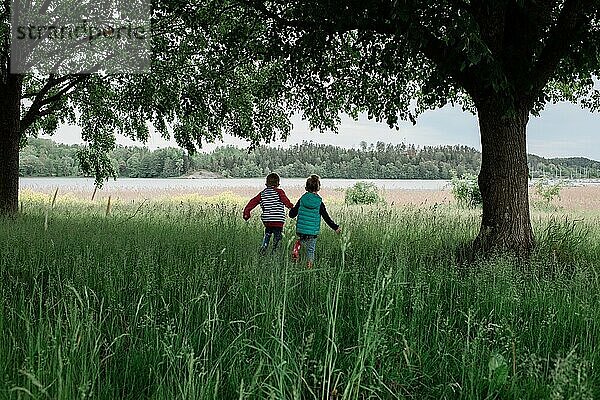 Junge und Mädchen laufen durch ein Feld zum Wasser