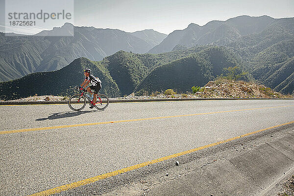 Ein Mann fährt mit dem Fahrrad auf einer Straße in einer bergigen Landschaft. Queretaro  Mexiko.