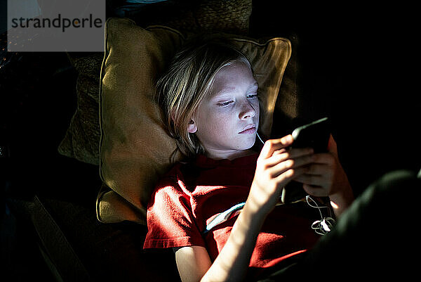 Kleiner Junge schaut im Dunkeln auf sein Smartphone