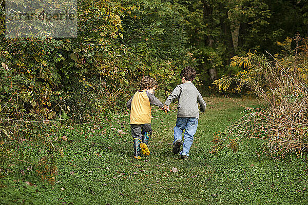 Dahinter sind zwei kleine Jungen zu sehen  die sich an den Händen halten und durch den Park rennen