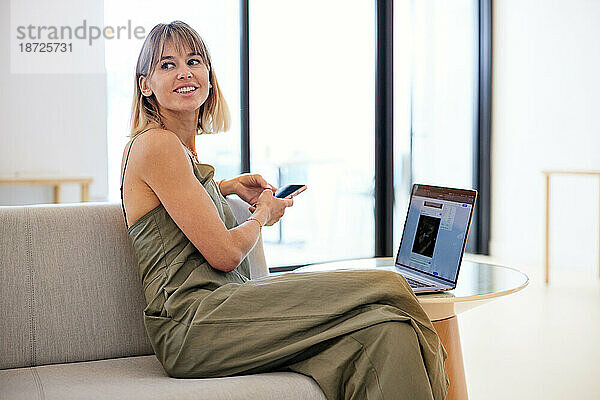 Lächelnde Geschäftsfrau schaut weg  während sie auf dem Sofa im Café sitzt
