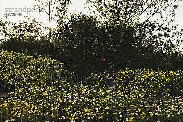 Landschaftsansicht eines kleinen Mädchens  das im Frühling durch ein Blumenfeld geht