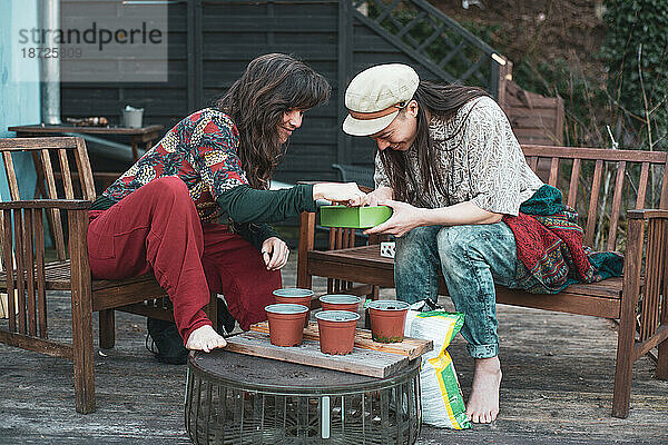 Lesbisches Paar lacht  während es Frühlingstopfpflanzen im Garten bepflanzt