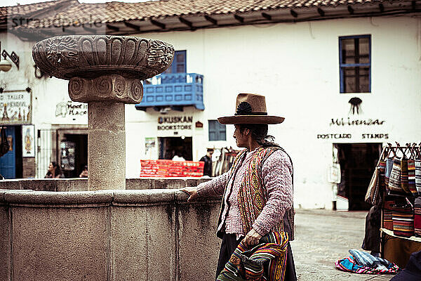 Einheimische peruanische Frau steht auf Kunsthandwerksmarktplatz mit Inka-Gebäude
