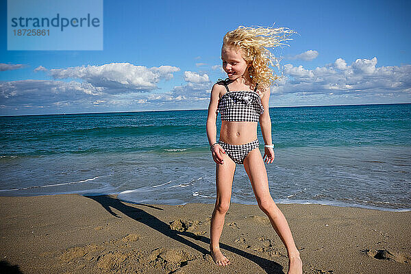 Lächelndes Mädchen  das am Strand steht  Wind weht Haare  blauer Himmel