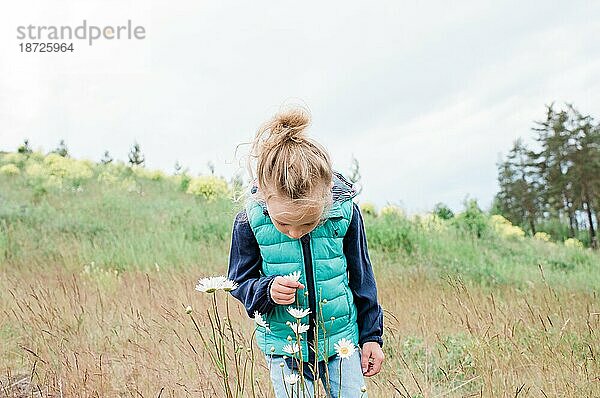 Junges Mädchen steht auf einem Feld und betrachtet eine Blume