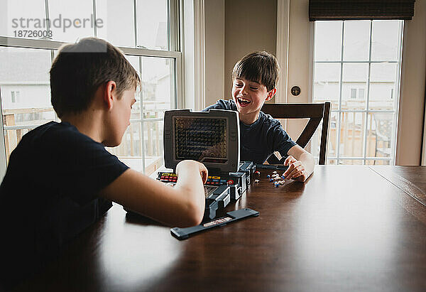 Junge lacht über seinen Bruder  während sie zusammen ein Brettspiel spielen.