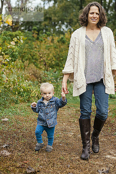 Eine Mutter und ein Kleinkind gehen im Herbst Händchen haltend gemeinsam durch einen Park