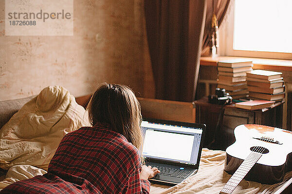 Junge Frau benutzt Laptop  während sie zu Hause im Bett liegt