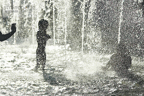 Silhouette von Kindern  die sich während einer Hitzewelle in einem Brunnen abkühlen