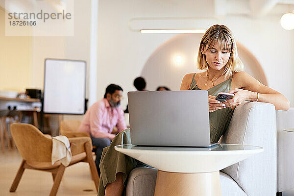 Geschäftsfrau sitzt mit Smartphone auf Sofa im Café