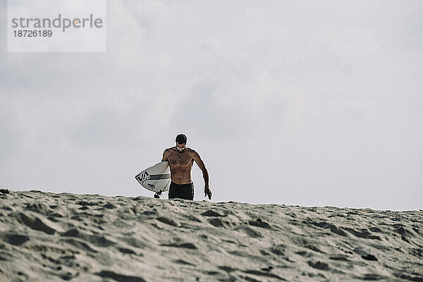 Zurückgezogene Ansicht eines Surfers  der auf Sand läuft