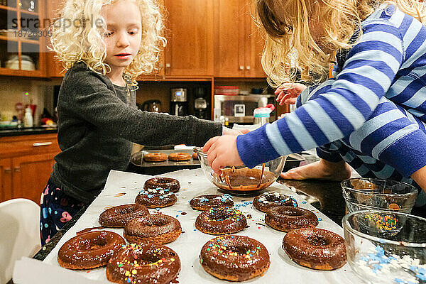 Nahaufnahme von zwei Kindern  die an der Küchentheke Donuts machen