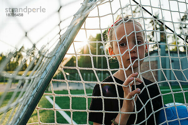 Mädchen stand auf dem Tor und hielt einen Fußball in der Hand  der durch das Tornetz schaute
