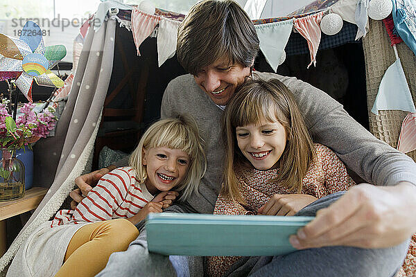 Father with happy daughters watching video on tablet computer