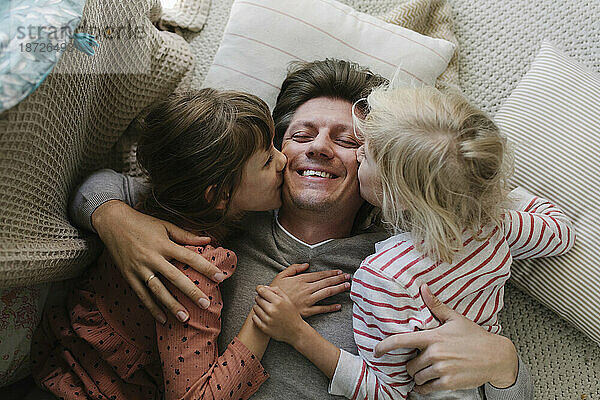 Daughters kissing father lying on pillow at home