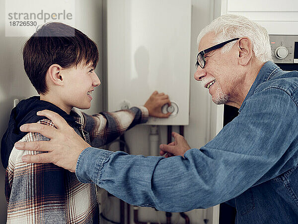 Lächelnder Enkel und Großvater passen den Heizkessel an  um zu Hause Energie zu sparen
