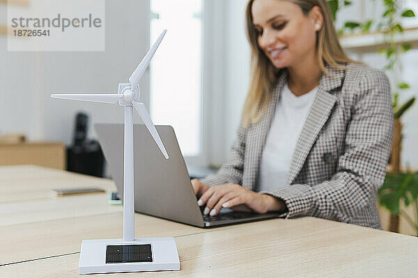Junge Geschäftsfrau nutzt Laptop und digitales Tablet am Schreibtisch  im Vordergrund ein Windkraftanlagenmodell