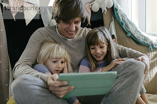 Vater mit Töchtern schaut sich Videos auf Tablet-Computer an