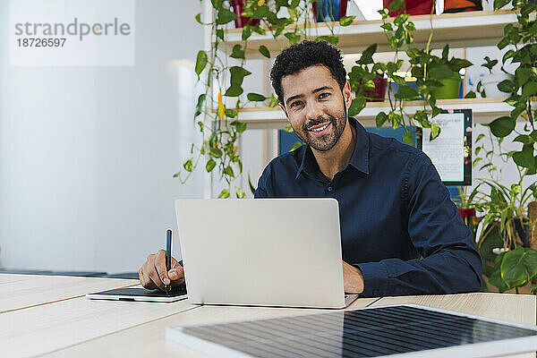 Porträt eines lächelnden Geschäftsmannes mit digitalem Tablet  Laptop und Solarpanel auf dem Schreibtisch