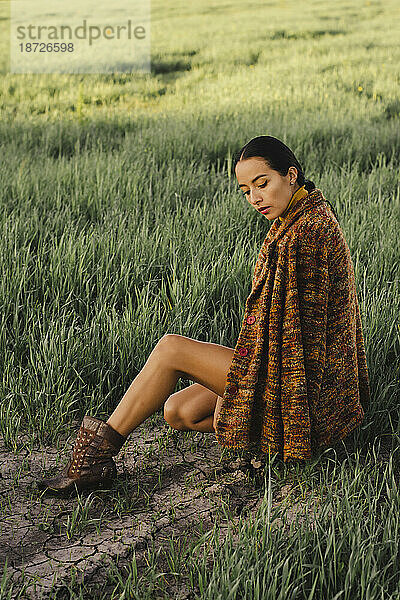 Young woman in long coat crouching in grassy meadow