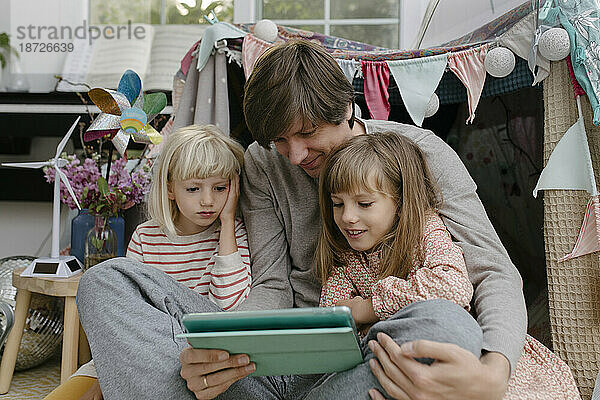 Vater mit Töchtern schaut sich Videos auf Tablet-Computer an