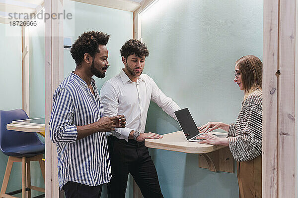 Geschäftskollegen arbeiten mit Laptop in Bürokabine zusammen