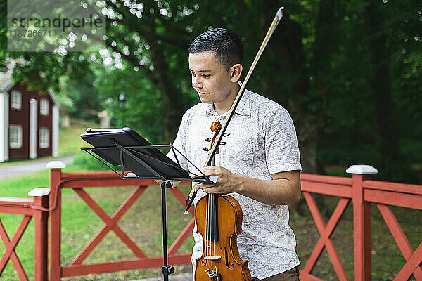 Mann hält Geige und liest Noten im Park